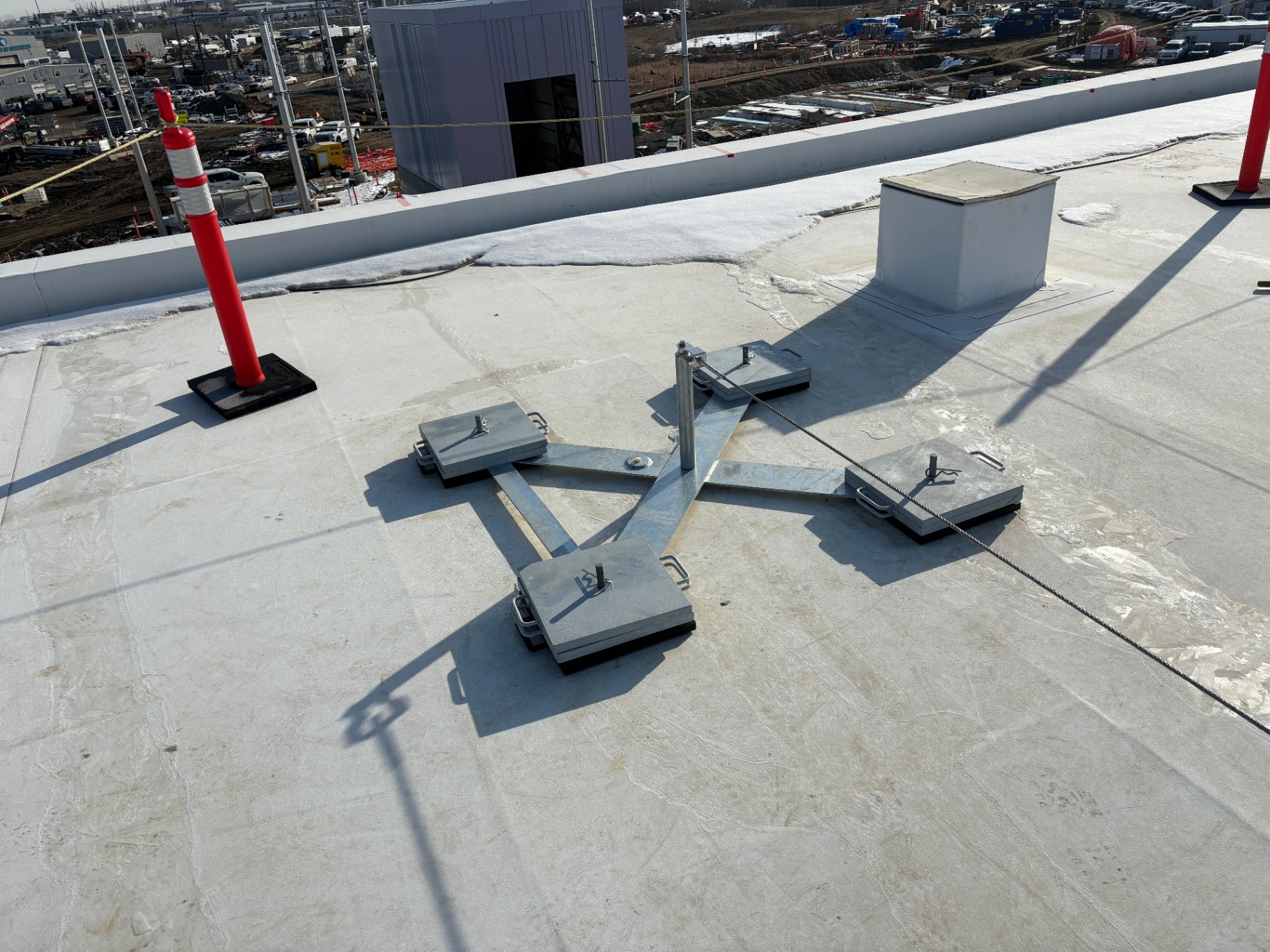 Horizontal lifeline corner run routed across a flat roof using non-penetrating counterweighted anchors