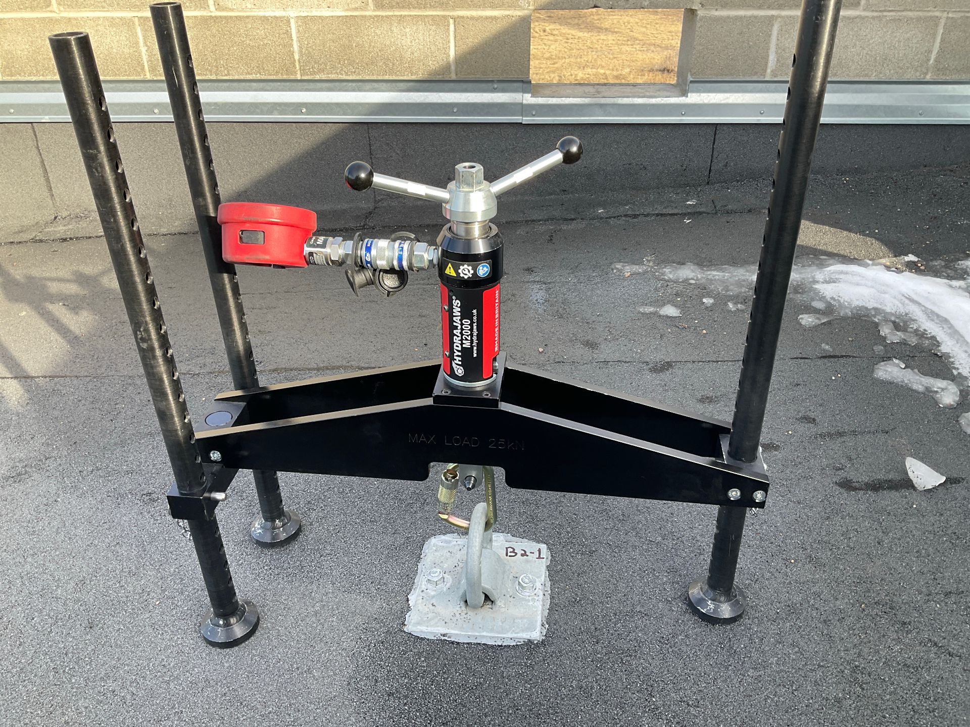 Single-point roof anchor under pull test with Hydrajaws proof-loading frame and digital gauge