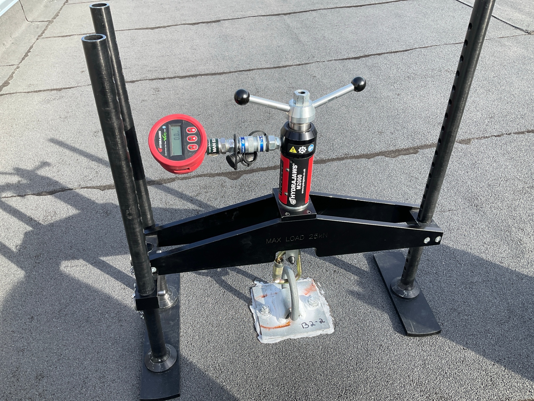 Hydrajaws pull-testing rig connected to a single-point roof anchor during proof-load verification on a flat roof