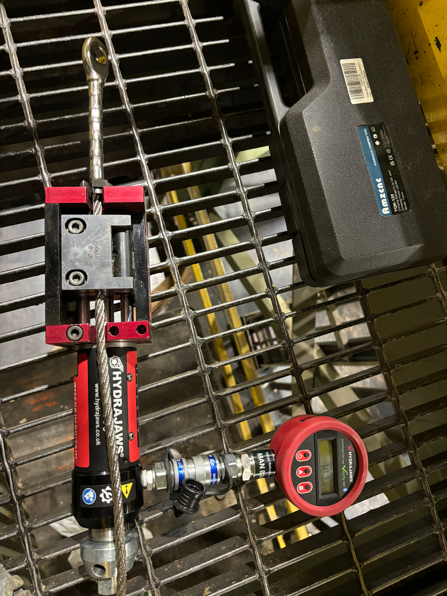 Eye-terminated swaged cable being load tested on industrial grating with Hydrajaws gauge reading