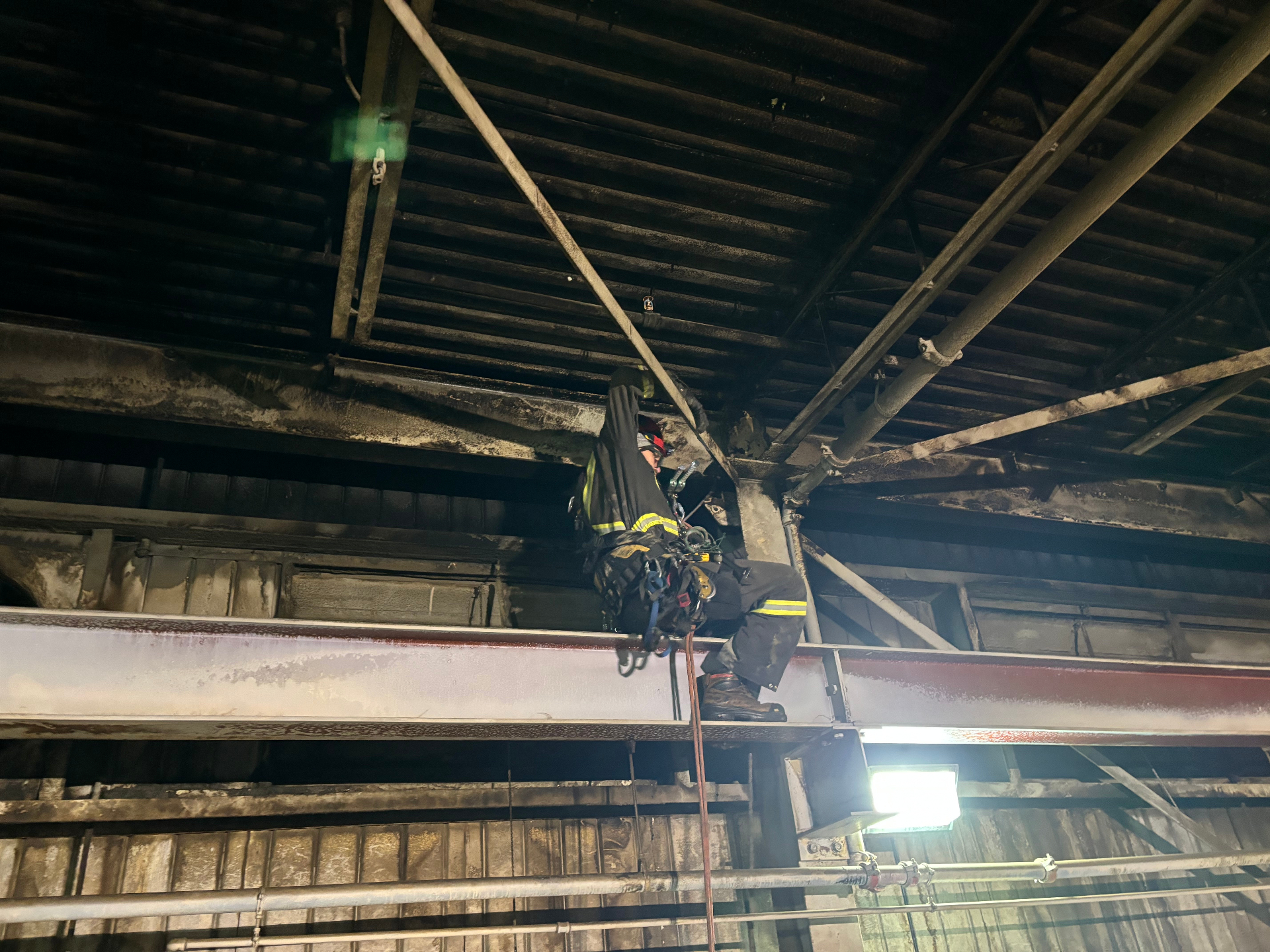 Rope access technician working off structural steel to reach an overhead sprinkler head inside an industrial facility