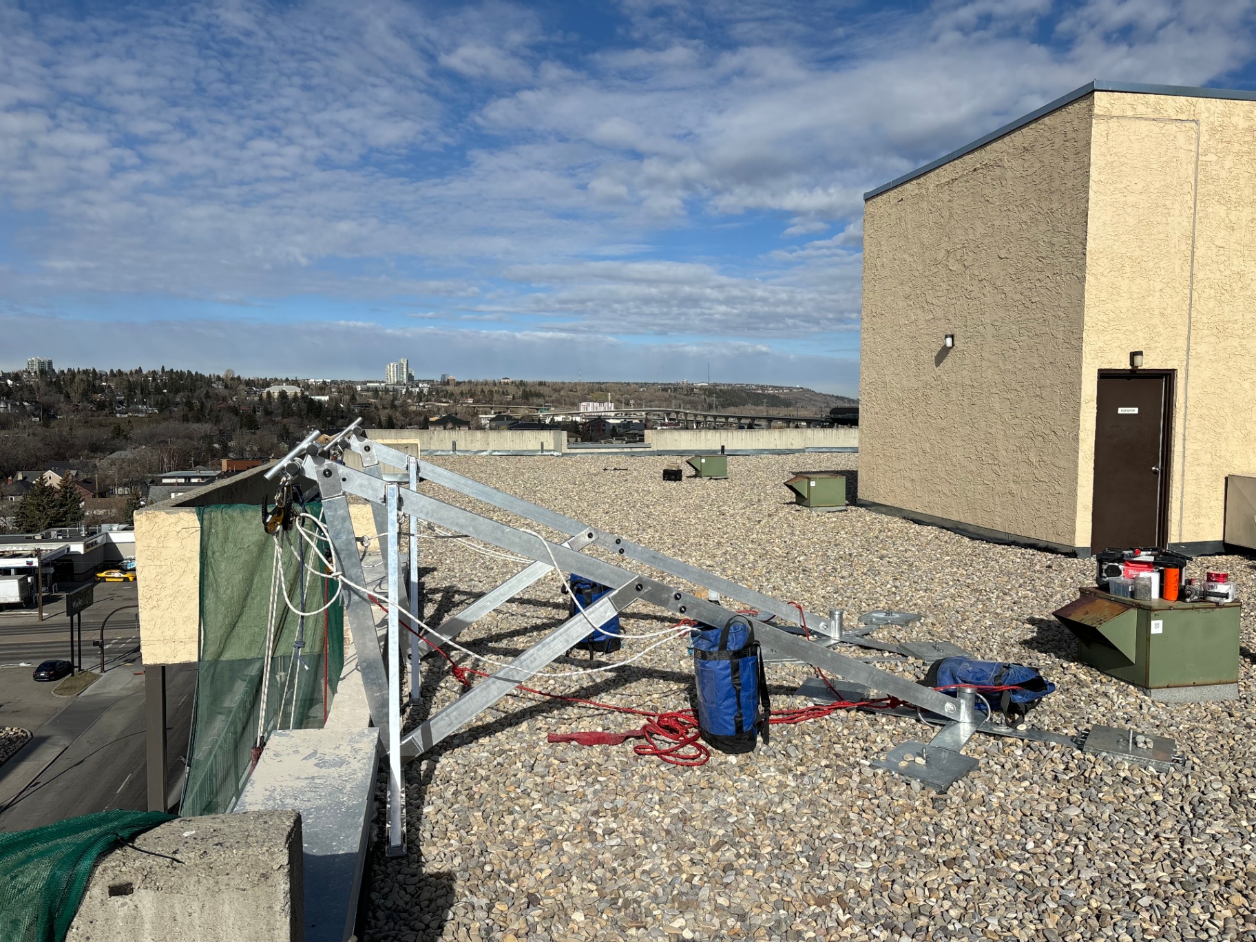 Non-penetrating davit-style anchor staged at a rooftop parapet with ballast bags and rigging