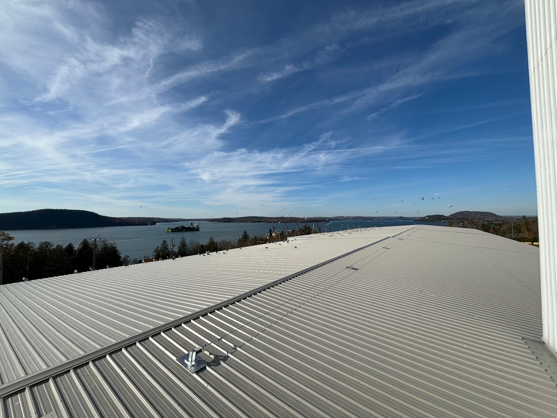 Long run of horizontal lifeline cable installed across a standing seam metal roof above the waterfront