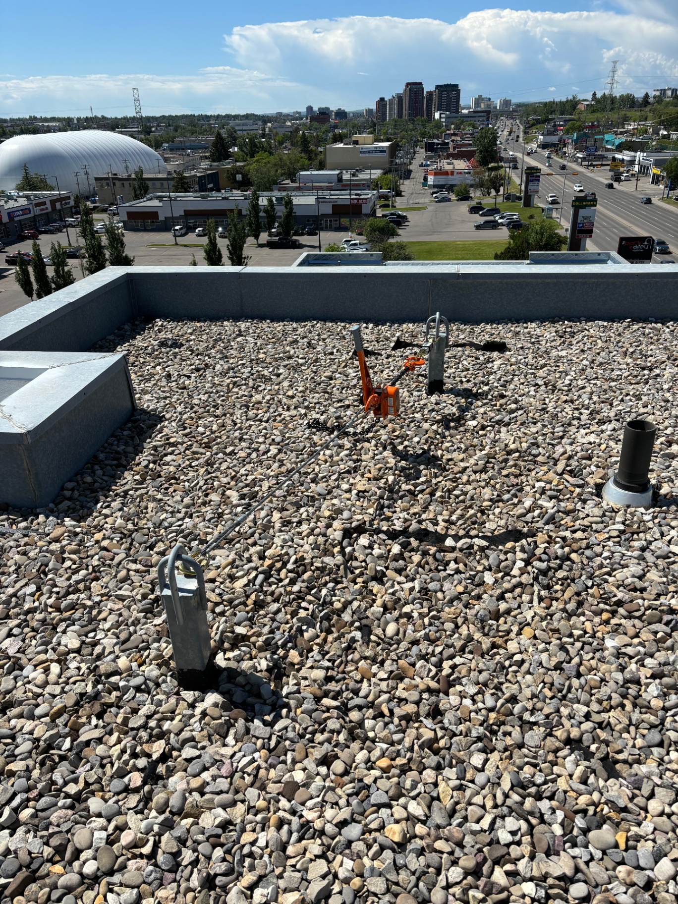 Pull-test chain hoist rigged between two single-point roof anchors on a gravel rooftop with a Calgary skyline beyond