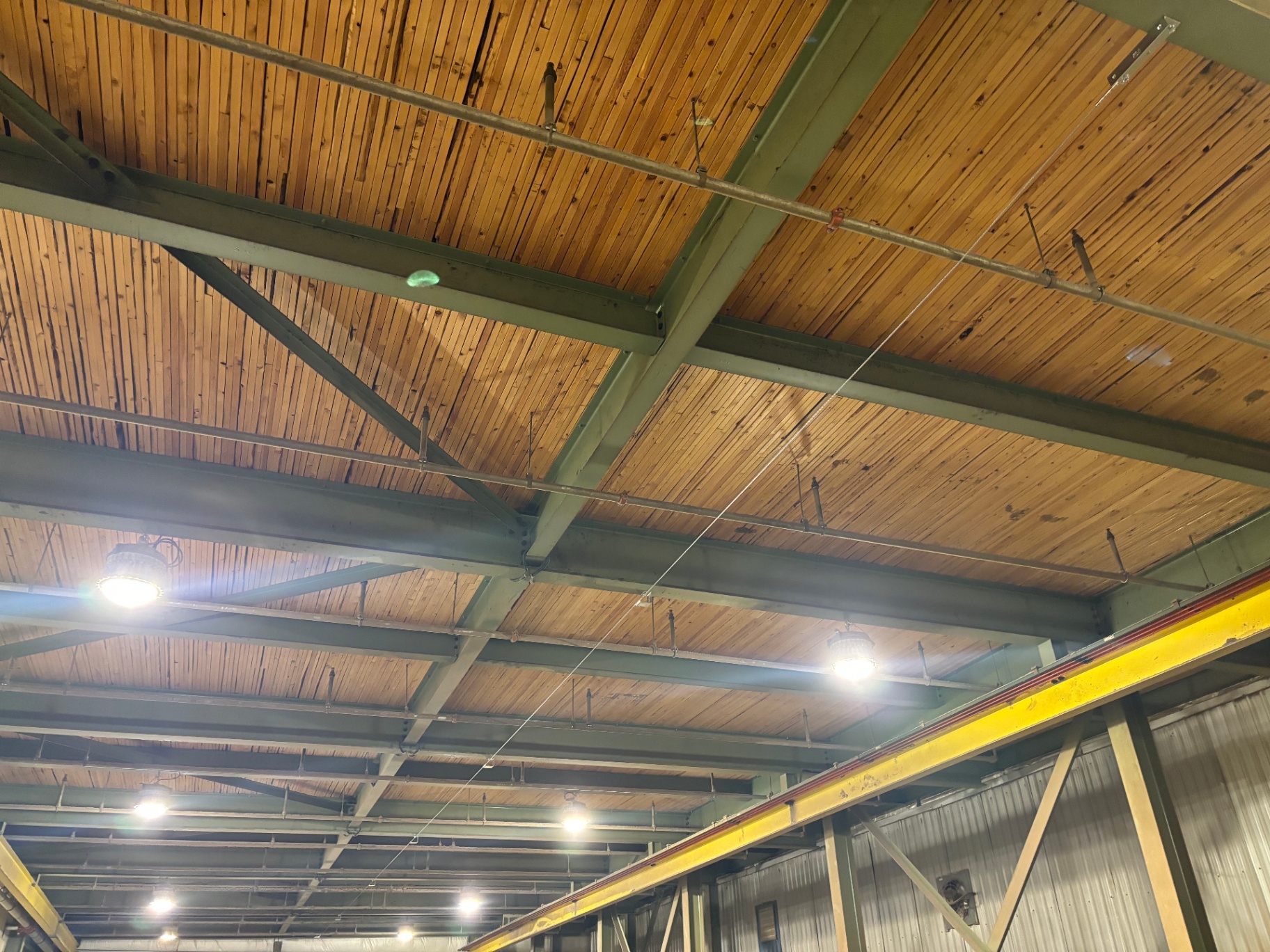 Overhead horizontal lifeline cable strung across an industrial wood-deck ceiling between steel beams