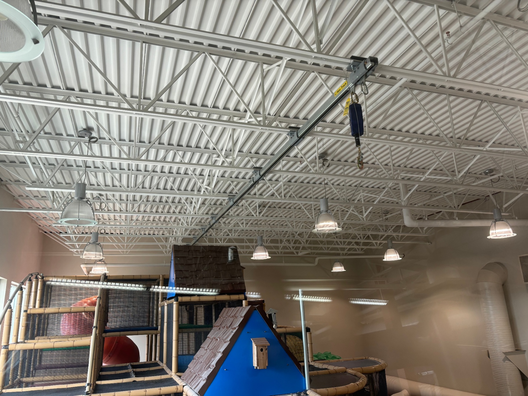 Overhead rigid track with articulating jib arm and self-retracting lifeline extending out over an indoor playcentre