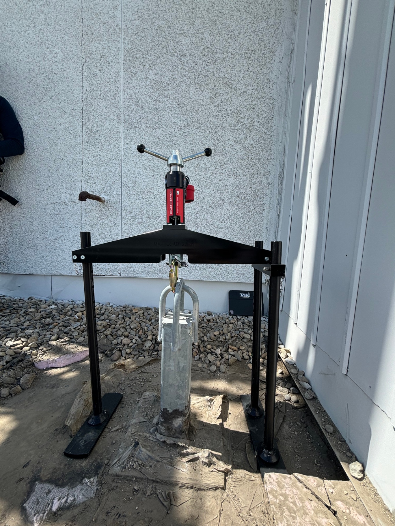 Tripod-mounted Hydrajaws hydraulic pull-tester set over a wall-mounted single-point anchor for vertical proof loading