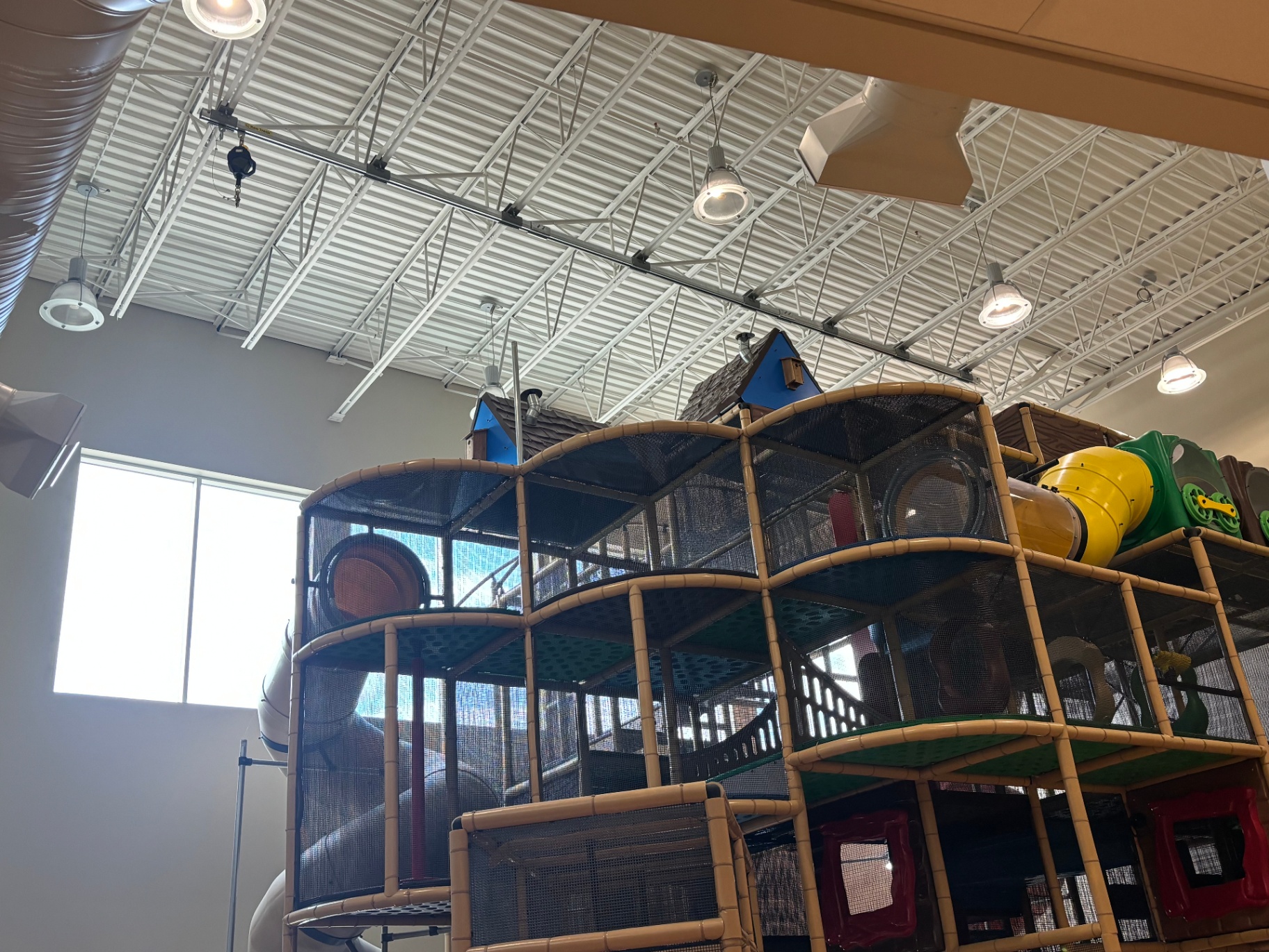Curved overhead rigid track fall arrest system with self-retracting lifeline installed above an indoor playcentre structure