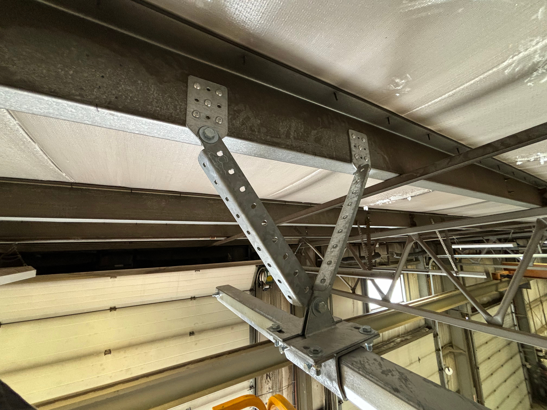 Overhead track fall arrest anchor bracket riveted directly into steel purlins inside an industrial building
