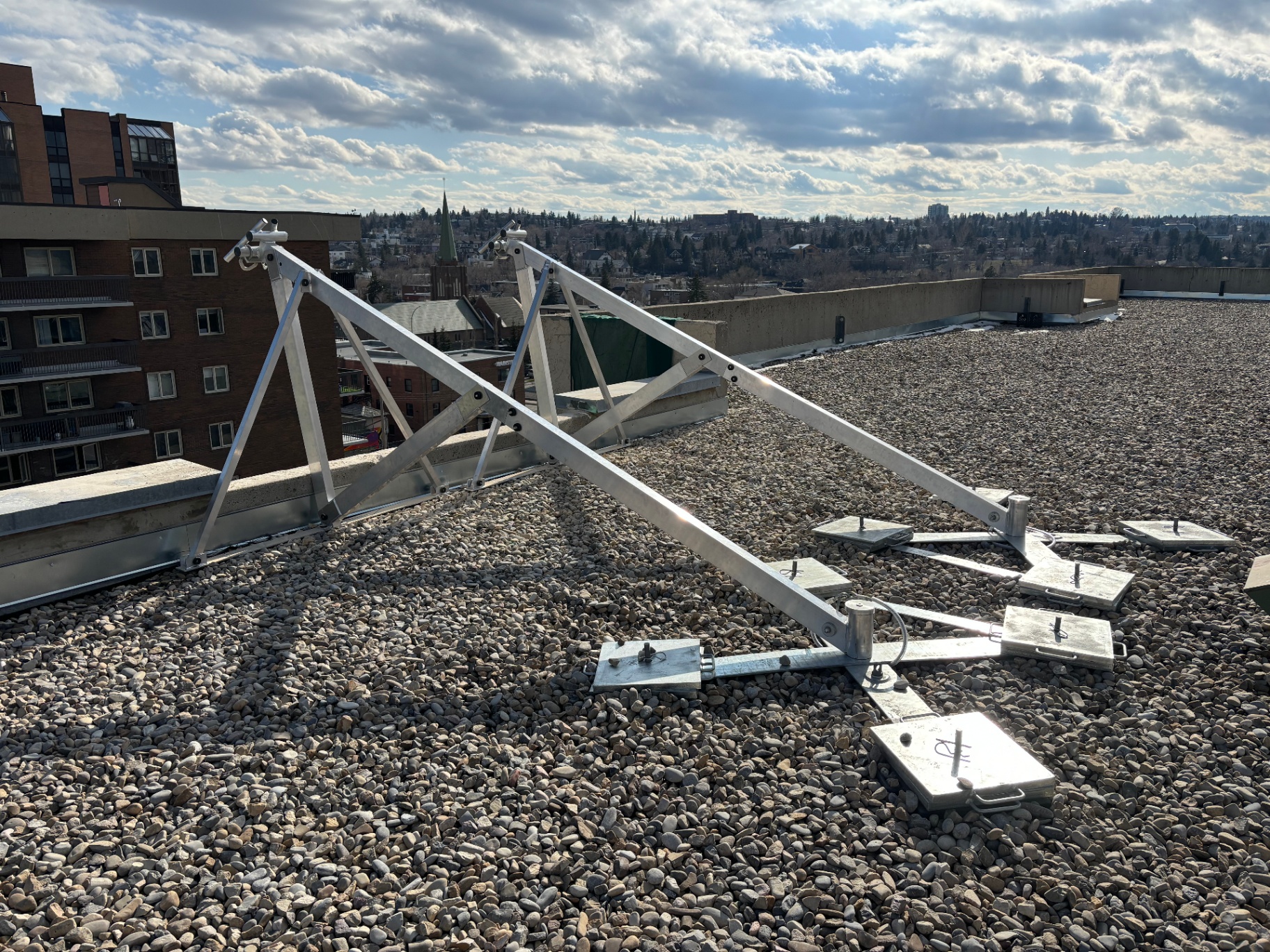 Non-penetrating ballasted roof anchor frame set on a gravel rooftop with concrete counterweights