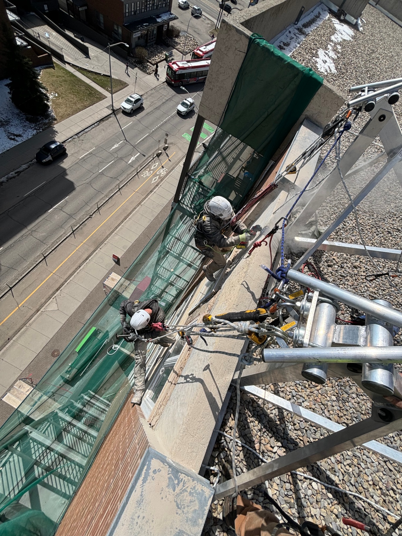 Rope access technicians working off a non-penetrating roof anchor at a downtown building parapet
